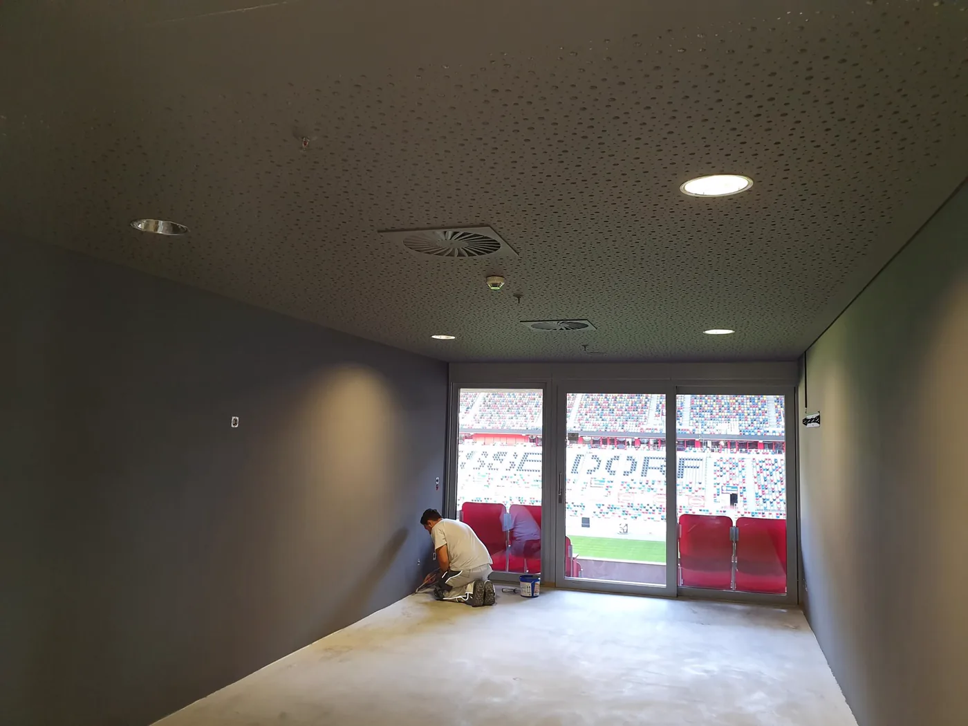 VIP-Lounge im Stadion während der Ausführung, Wandflächen werden gespachtelt, Blick durch die Fensterfront auf die Tribüne